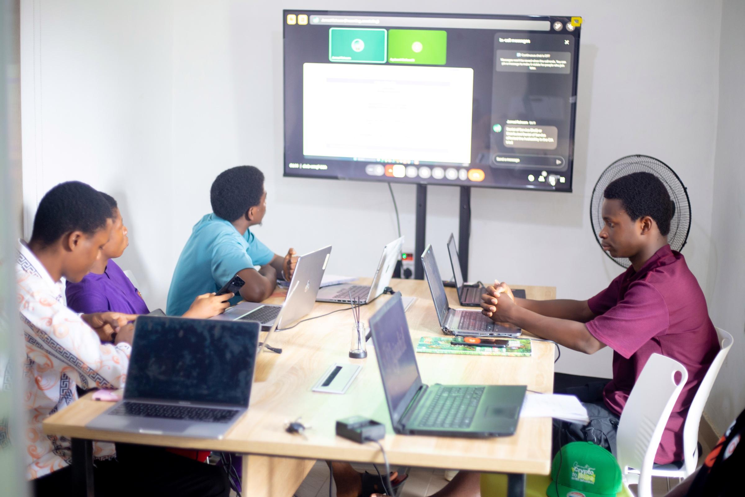 A class in session at Haut Hub: students with laptops around a table, facing a large screen