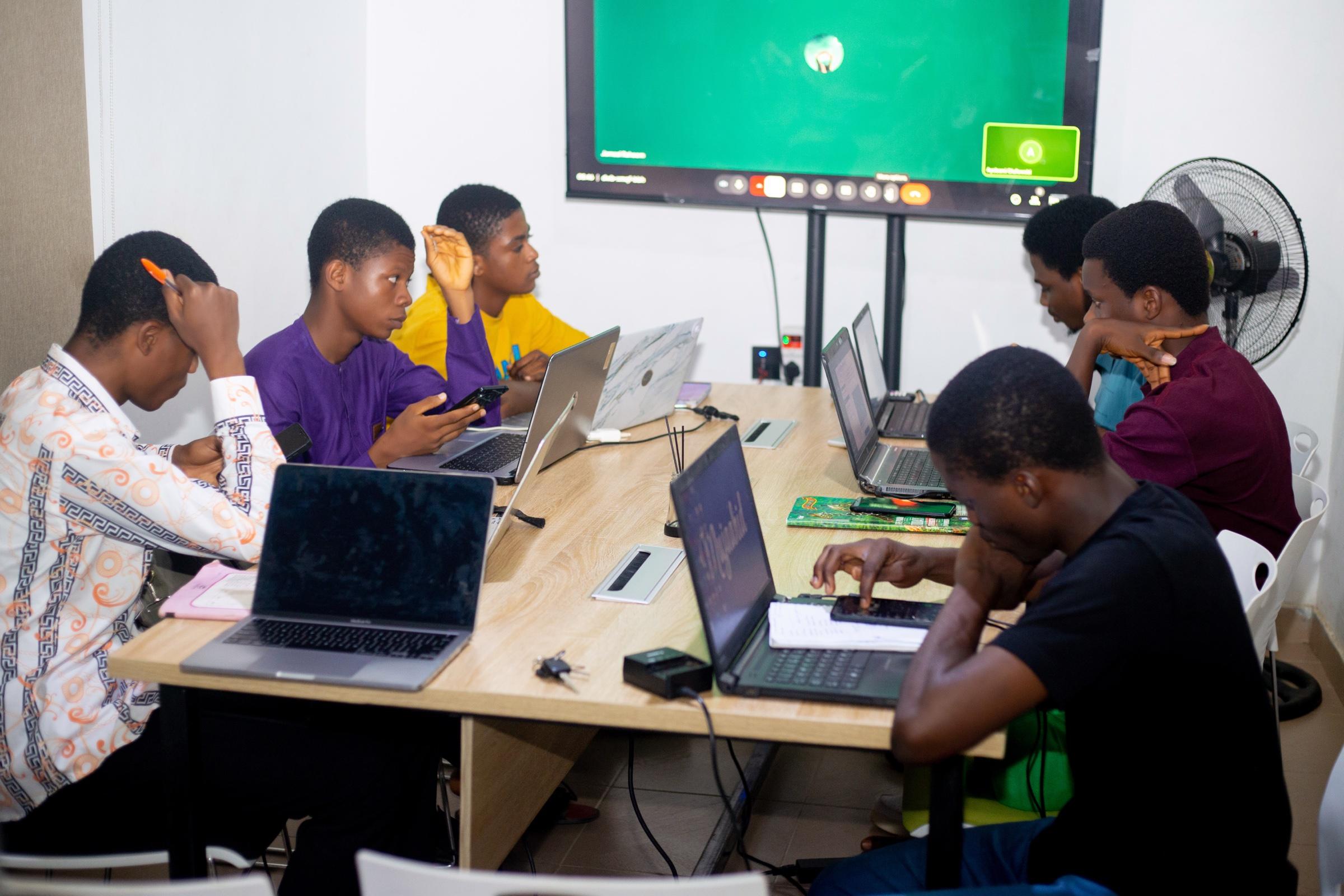 Students working at their laptops and phones around the classroom table